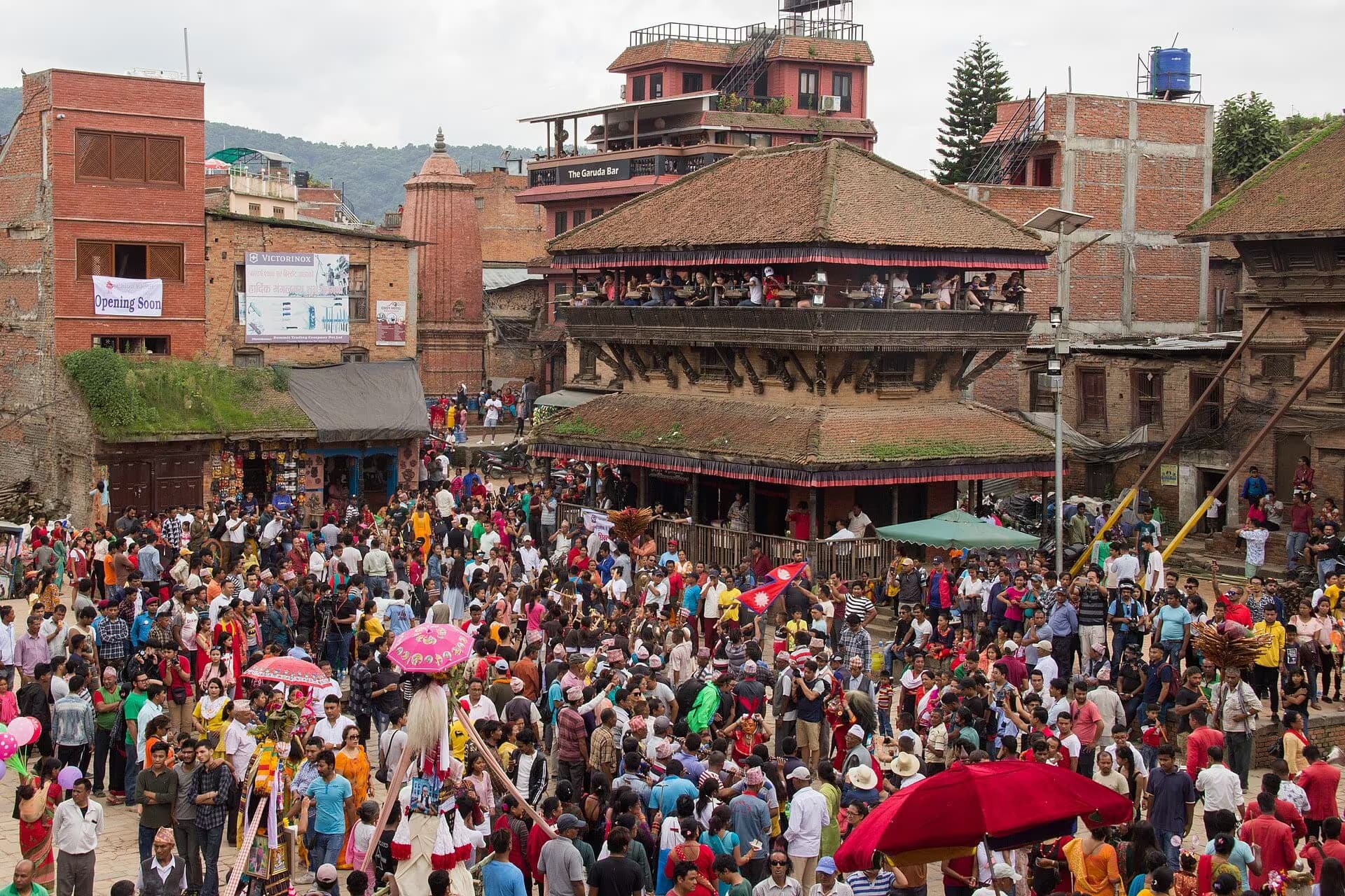A Gai Jatra procession filling a Bhaktapur square, bright parasols above the crowd