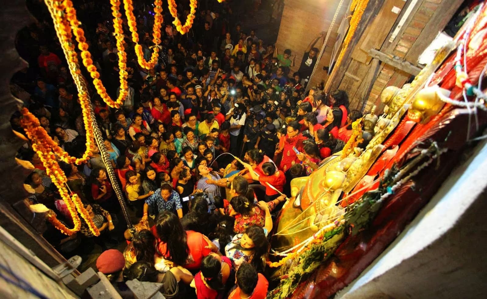 A crowd pressing around Swet Bhairav's gilded mask under marigold garlands at night