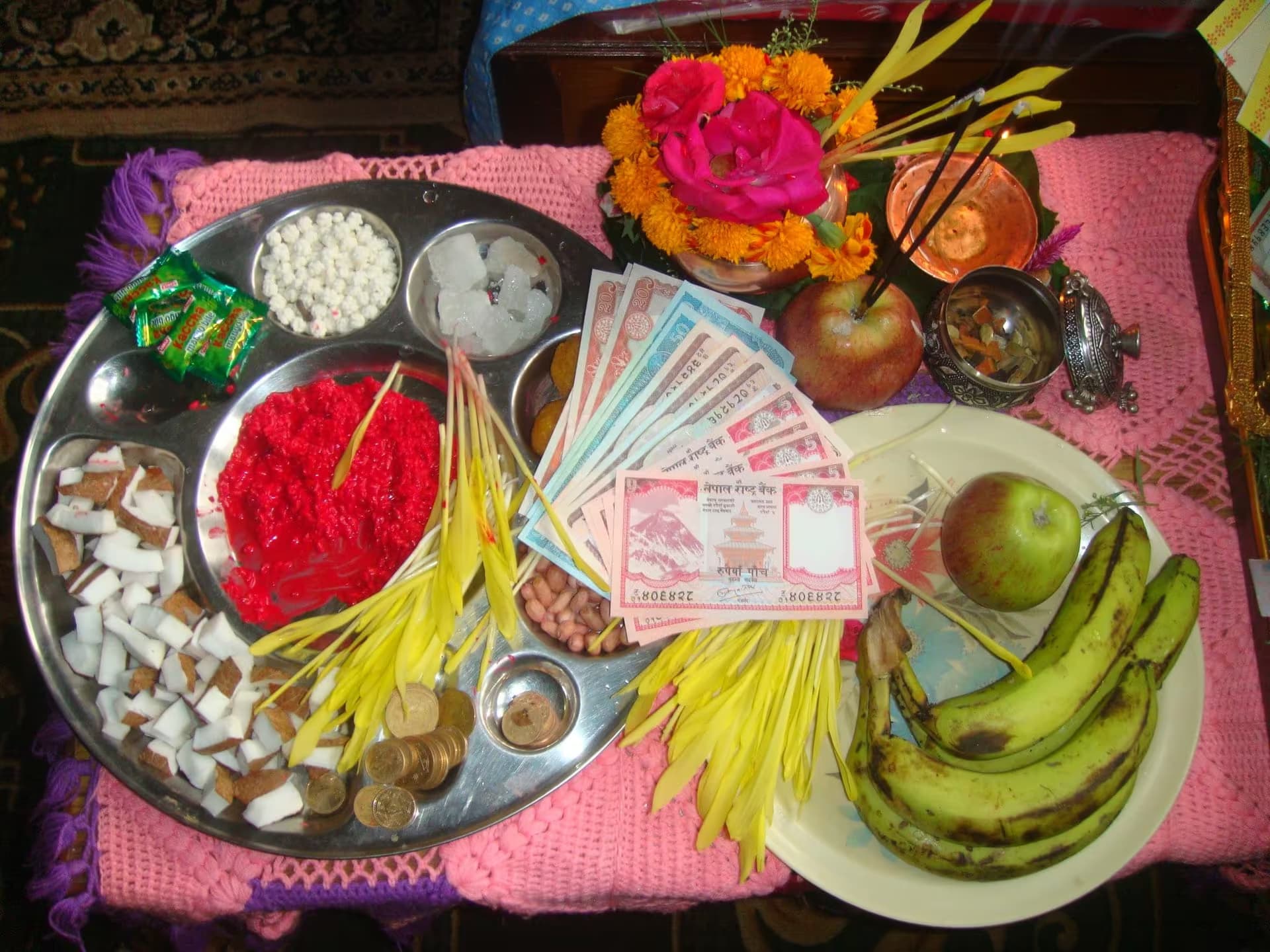 A brass thali laid out for Dashain tika with red tika, jamara, coconut, coins and rupee notes