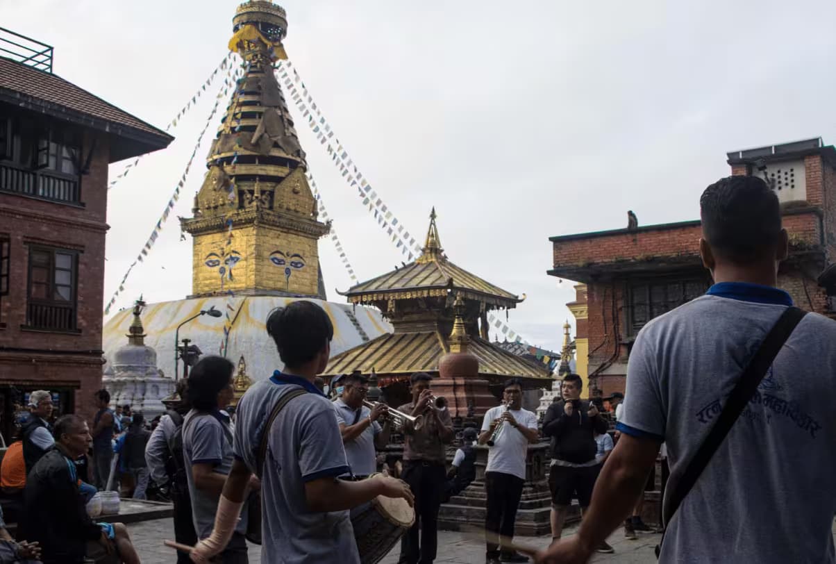 Drummers and long-horn players performing below the gilded spire of Swayambhunath stupa on a monsoon morning