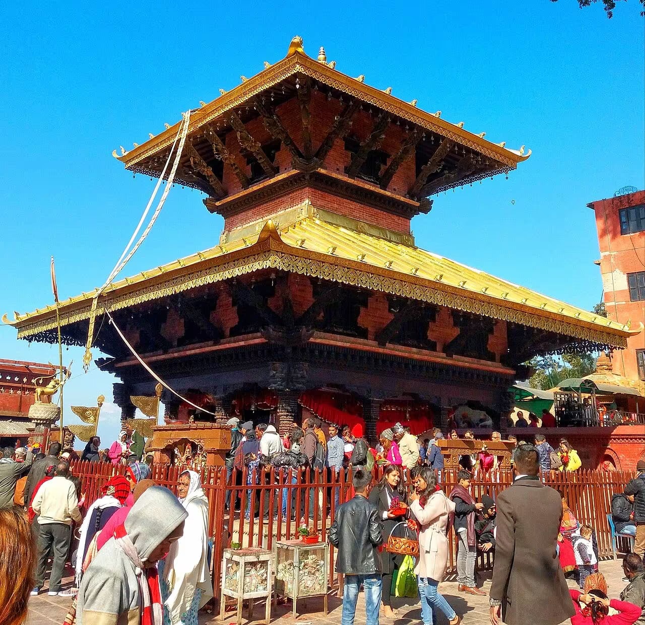 Crowds of pilgrims around the gilded pagoda of Manakamana Temple, with Himalayan peaks behind